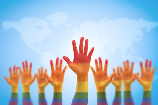 Rainbow multi-color flag pattern on many people's hands isolated on blue sky world map (clipping path)