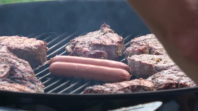 Man's hands cooking steak and sausage on grill