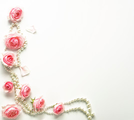 A frame of pink roses and beads on a white background.Top view. Copy space