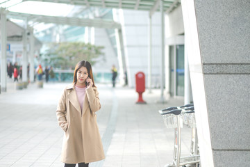 arming beautiful asian business woman smile in casual style using smartphone for travel with blur the airport terminal.