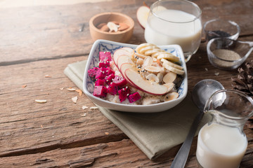 Bowl of oatmeal porridge with bananas, apple, dragon fruit and almonds. Top view
