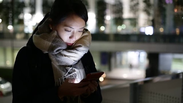 Young Asian Woman texting on cellphone in city at night