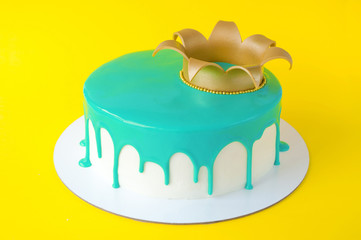 Cake baking with turquoise glaze decorated with gold crown on yellow background. Picture for a menu or a confectionery catalog.