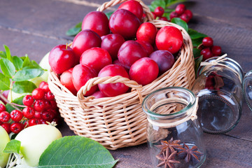 Fototapeta na wymiar Plums in a basket, apples, rowanberry and glass jars 