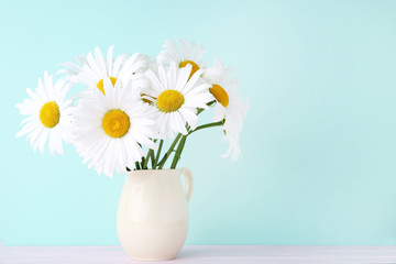 Bouquet of chamomile flowers in jug on mint background