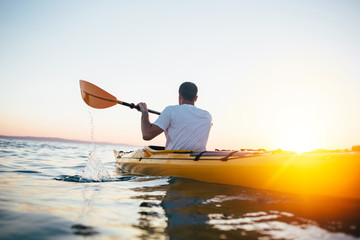 Man paddling the kayak at sunset - obrazy, fototapety, plakaty