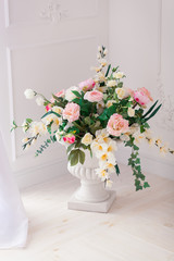 A bouquet of peonies and roses in a clay white jug on the floor at the threshold of the French window. Bright interior