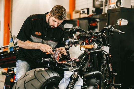 Professional motorcycle mechanic works with electronics, cuts wires. Handsome mechanic working in bike repair shop.