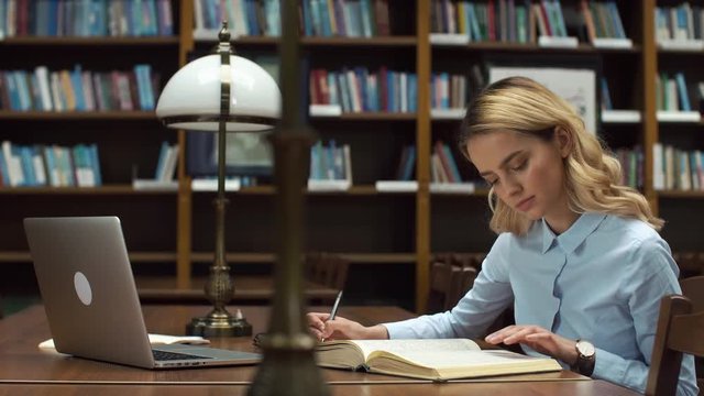 Student works with books and laptop in the library