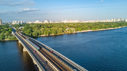 Obraz premium Aerial top view of Metro railway bridge with train and Dnieper river from above, skyline of city of Kiev, Ukraine 