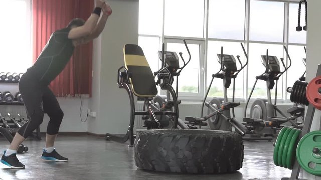 Slow motion of male fitness model training workout witth heavy and big tire and hammer in fitness center
