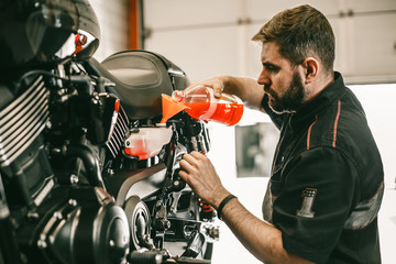 Professional mechanic pouring antifreeze into a motorcycle. Confident young man repairing motorcycle in repair shop.