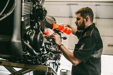 Professional mechanic pouring antifreeze into a motorcycle. Confident young man repairing motorcycle in repair shop.