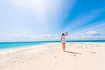 Fototapeta na wymiar beautiful smiling girl in hat on a beach of blue ocean and sky on the background