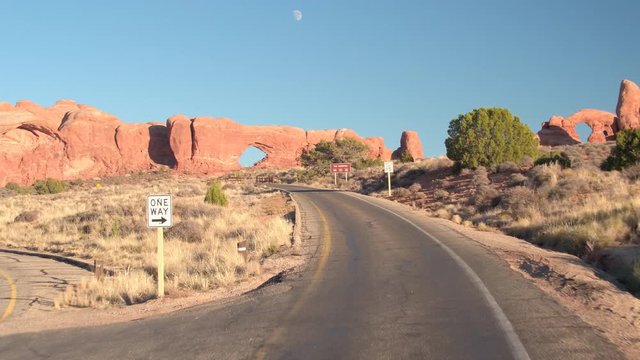 FIRST PERSON VIEW: Driving along an empty road through stunning Arches National Park in Utah on sunny day. Curvy road winding past the amazing red rock sandstone formations in hot desert United Stated