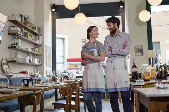 Two young restaurateurs holding tablet and smiling at each other