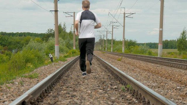 A man in sports uniforms runs on rails. He follows his health, runs cross, active life style.