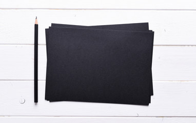 stack of black paper with pencil on a white wooden table