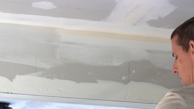 Homeowner puts joint compound over seam of drywall between wall and ceiling.