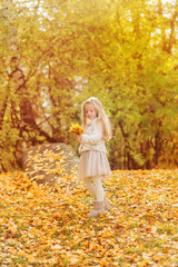 little girl in warm cardigan smiling against the background of fallen leaves