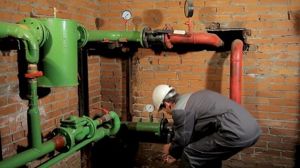A worker in overalls opens the water valve. plumber comes and opens the valve. The man includes heating in the boiler room. - Powered by Adobe