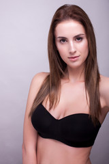 Portrait of woman in bra with natural make up on gray background in studio photo. Beauty and fashion.