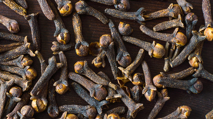 Clove spice scattered on a dark wooden surface close-up
