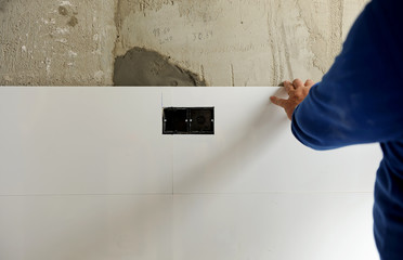 Construction worker putting white porcelain stoneware tiles in the kitchen