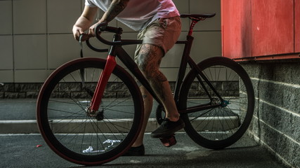 Tattooed biker hipster man in shorts winding the bar tape on a fixed gear bike handlebar