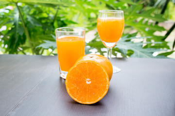 Close up of orange juice with cut and whole oranges on wooden table.