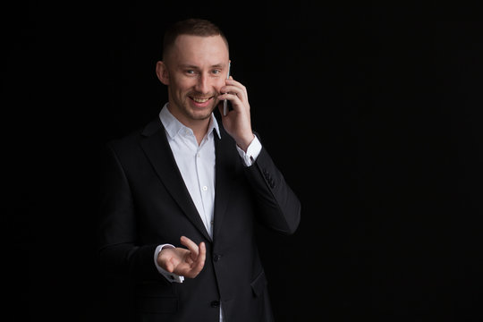 Young bisnessman talking by mobile phone isolated on black background.