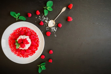 Panna cotta with syrup in a plate and raspberries with spoon on a dark background. Flat lay. Top view