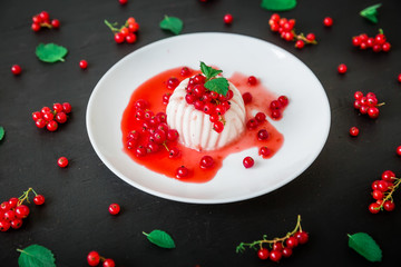 Panna cotta with red syrup in white plate on a dark table and currant berries. Italian dessert.