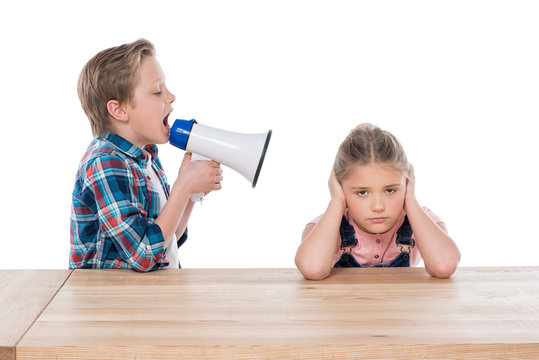 angry boy with megaphone yelling on his sad sister isolated on white