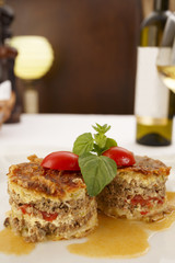 Moussaka arranged on a plate, Wine bottle and wineglass in background, Traditional dish in elegant setting, Selective focus with soft light