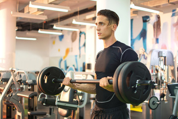 Fototapeta na wymiar Young strong man working out with barbells in gym.