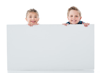 Two adorable siblings holding blank white banner and smiling at camera