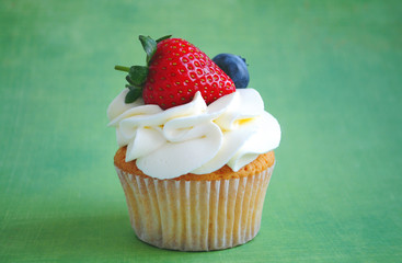 Cupcake with whipped cream, fresh strawberry, blueberry on green background. Picture for a menu or a confectionery catalog.