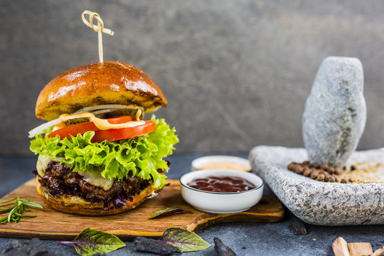 Tasty grilled glazed beef burger with lettuce and cheese served on wooden table with copyspace, blackboard in background.