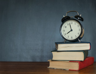 Books and an alarm clock stand on the background of a school board