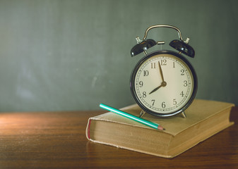 Books and an alarm clock stand on the background of a school board