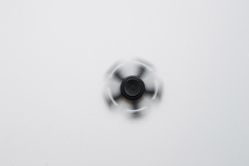 Black spinner on a white background. Black spinner with metal bearings spins on a white background. A toy made of aluminum alloy for fun and stress relief for an office worker and an ordinary employee