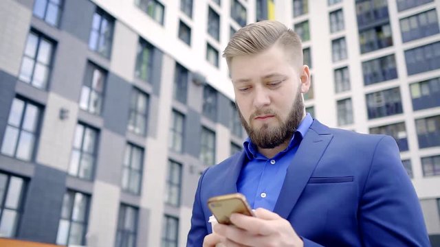 Businessman using electronic device is a mobile phone outside the building