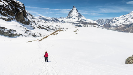 Fototapeta na wymiar ZERMATT, SWITZERLAND - May 16. 2017: Hiker walking on snow towards Matterhorn Mountain with white snow and blue sky in Zermatt city in Switzerland