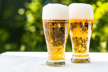 Two glasses of beer on a white wooden table.