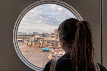 Girl looking through a round window at schiphol airport in amsterdam.