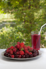 A house hamper of cherries, strawberries and raspberries in a glass. Plate with fresh fruit. Summer refreshing drink on a green background.