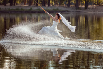 Bride sportswoman in a wedding dress is surfing on a lake. © Petro