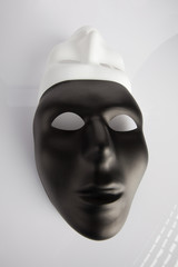 Black and white masks joined on white reflective background. Wide angle, vertical image, top view.