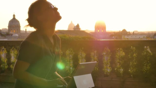 Young woman in campidoglio working on her laptop in front of Rome cityscape